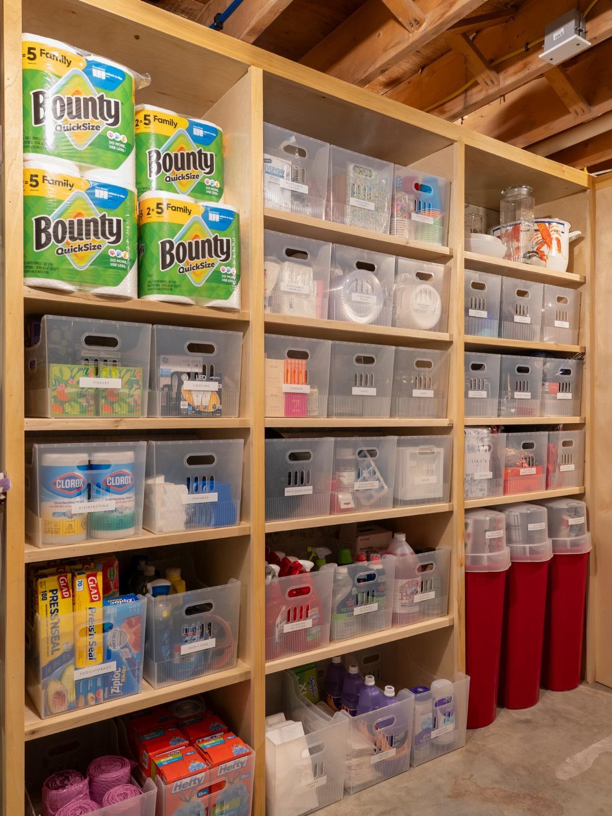 Wooden shelving units holding clear plastic storage bins and household supplies in a basement.