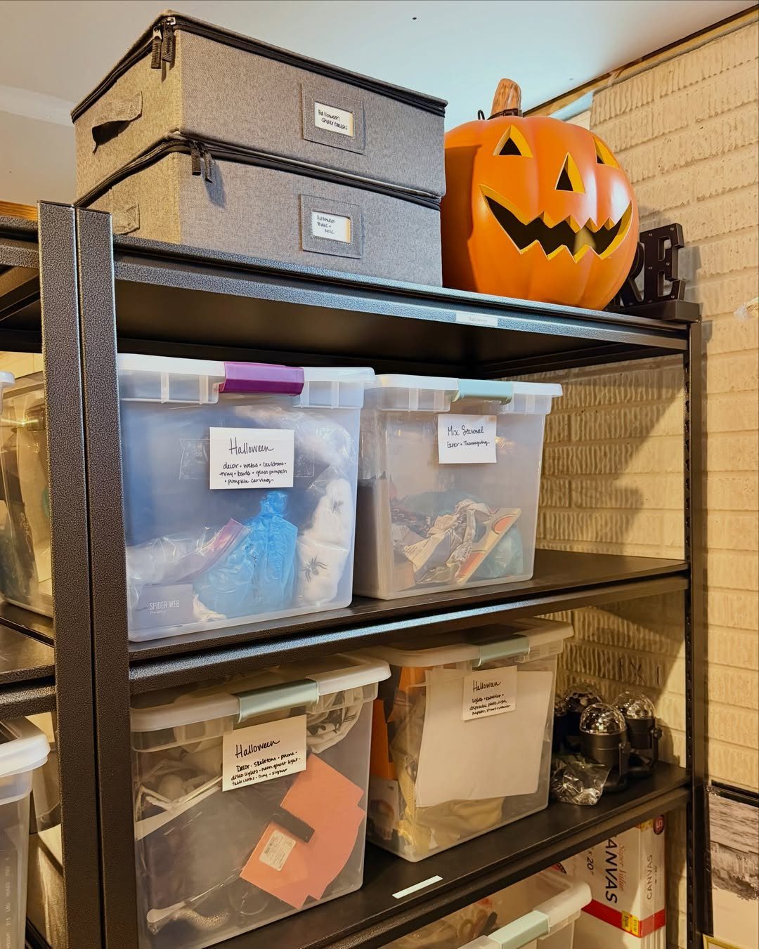 Clear plastic bins with labels and a pumpkin on black metal storage shelves.