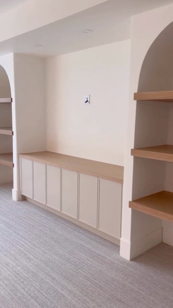 Built-in beige cabinets and arched wooden shelving units in a clean white room.