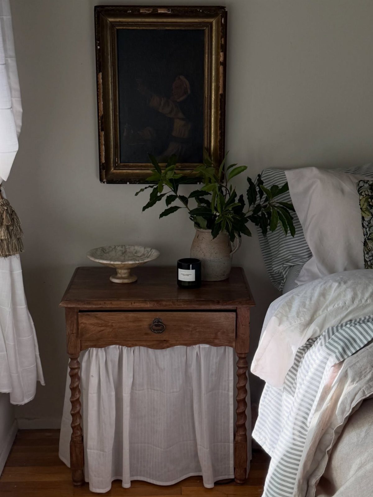 Wooden bedside table with a white fabric skirt and a single drawer.