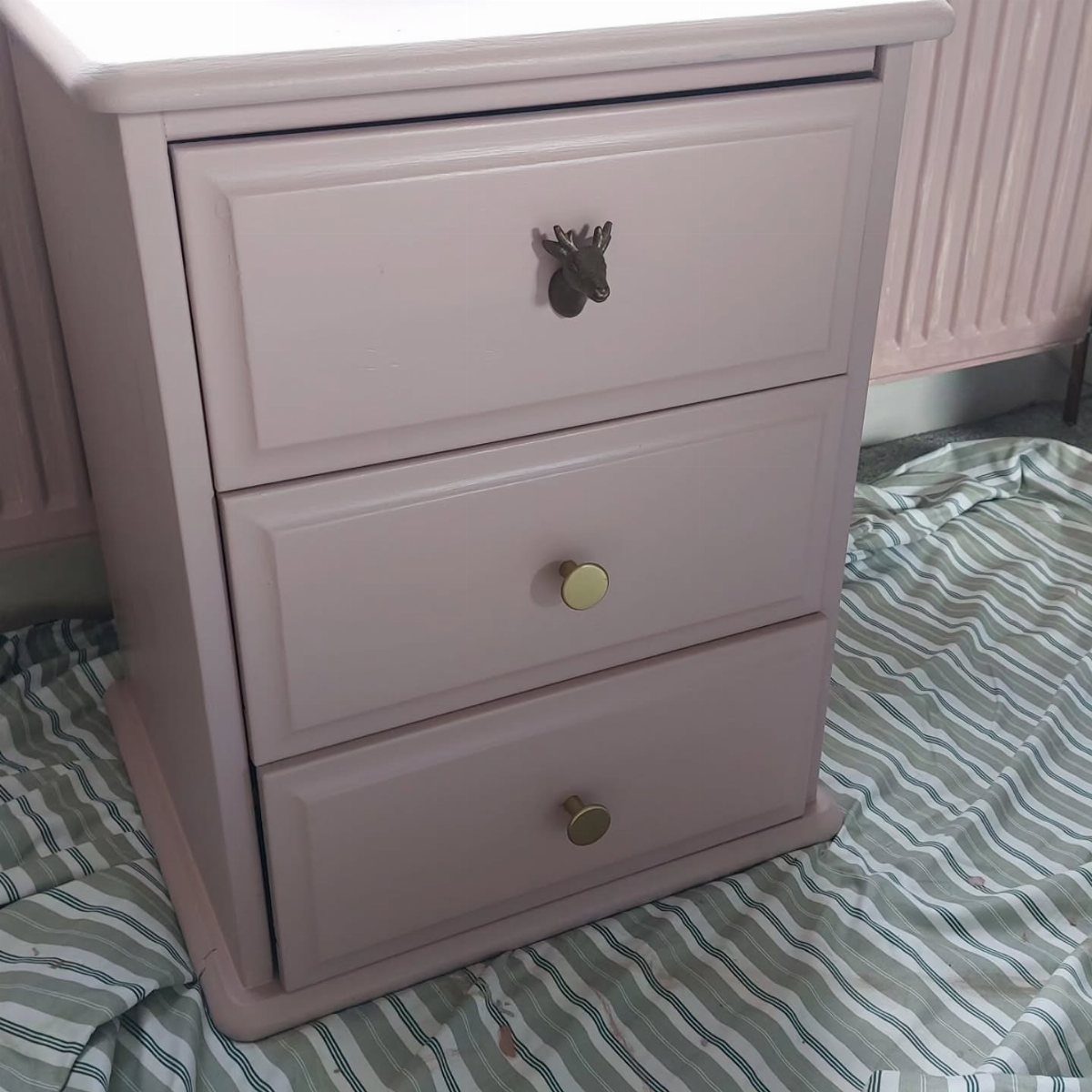 Pink three-drawer bedside table with a deer head pull and gold knobs.