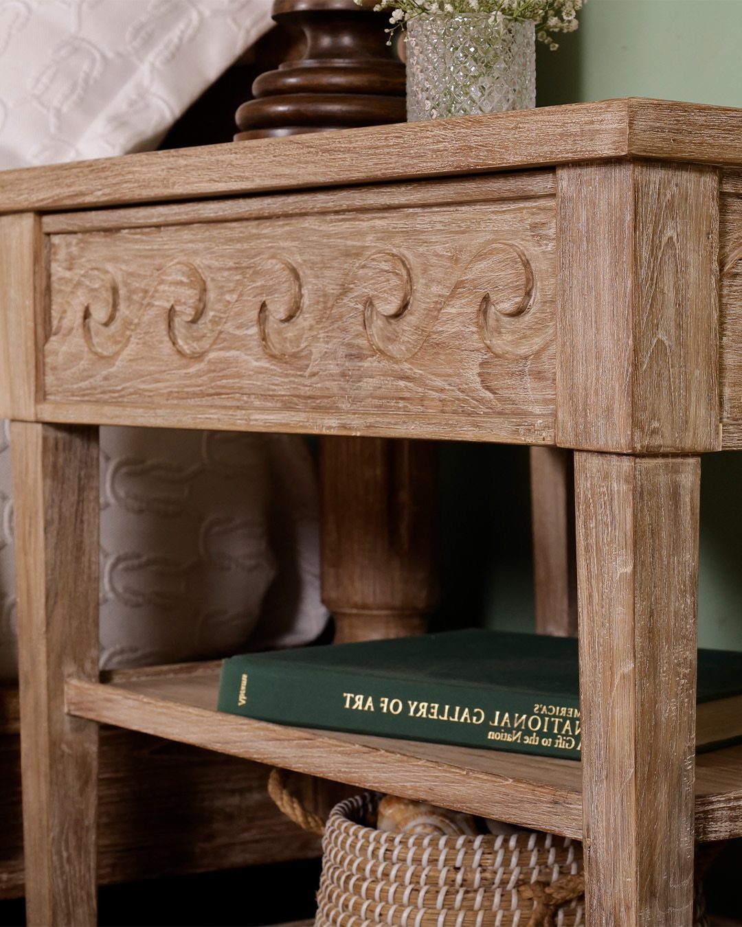 Wooden bedside table with carved details, a lower shelf, and a green book.