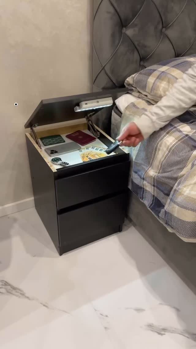 Dark brown bedside table with an open top compartment containing a smartphone and wallet.