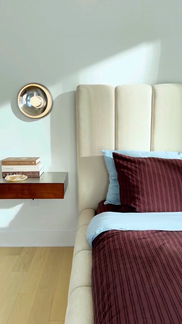 Dark wood floating nightstand mounted to a wall beside a cream upholstered bed.