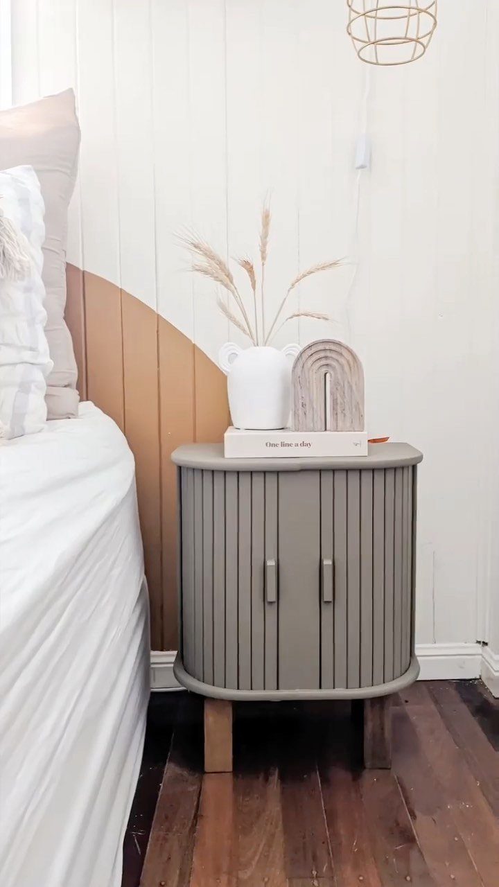 Grey fluted bedside table with light wood legs next to a white bed.
