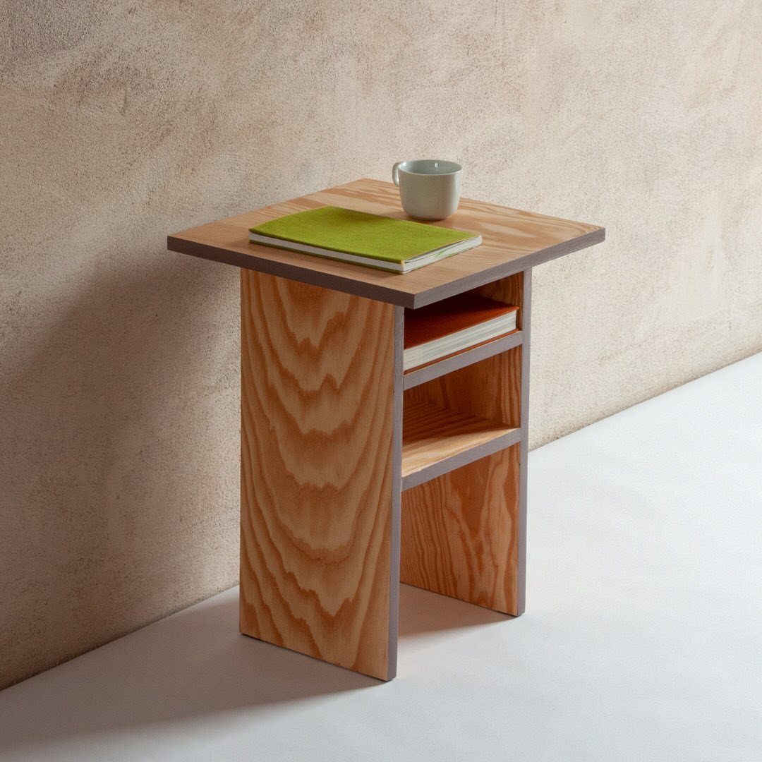 Wooden bedside table with a single shelf, green notebook, and grey cup.