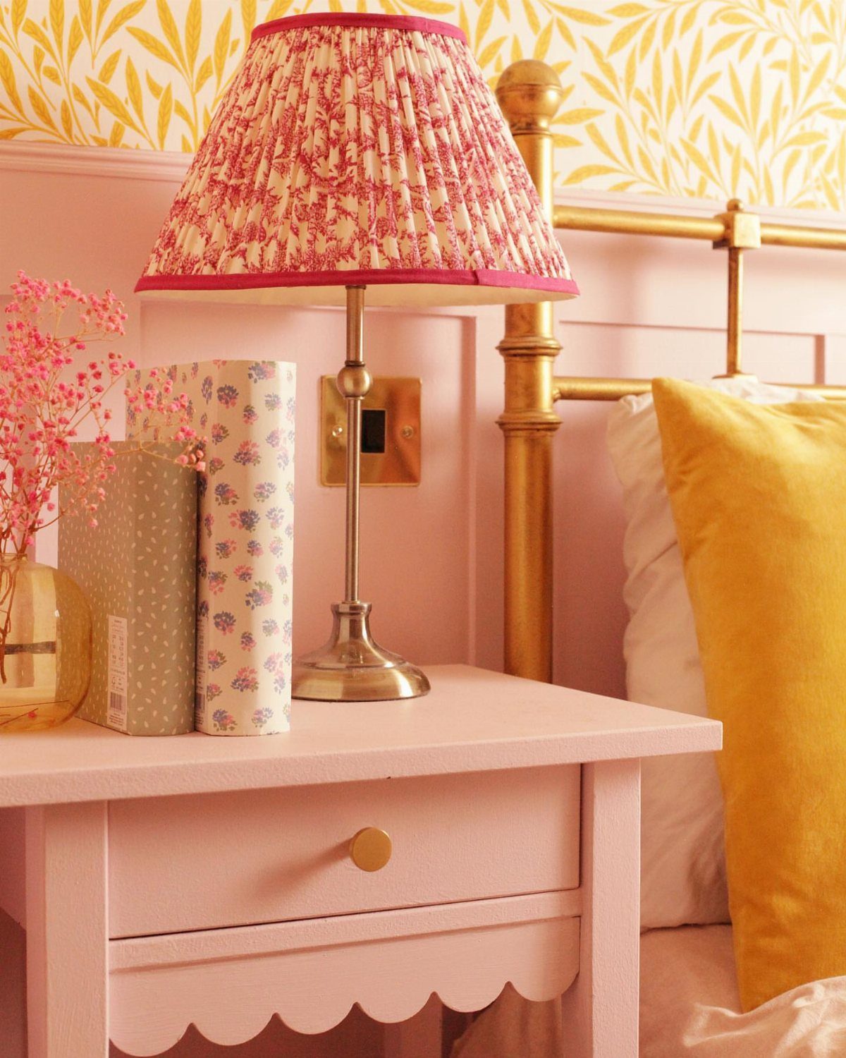 Pink wooden bedside table with a scalloped edge and a floral lamp.