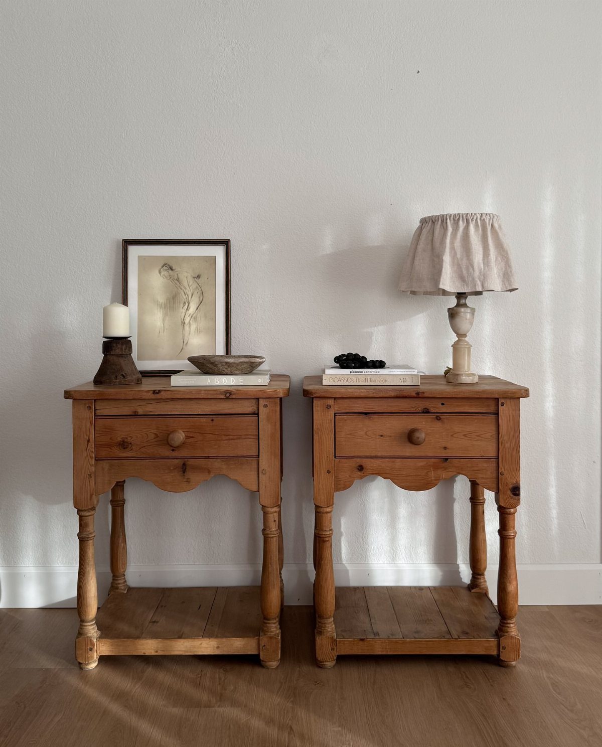 Two wooden bedside tables with drawers and turned legs against a white wall.