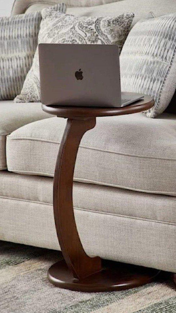 Round wooden C-shaped side table with a laptop next to a beige sofa.