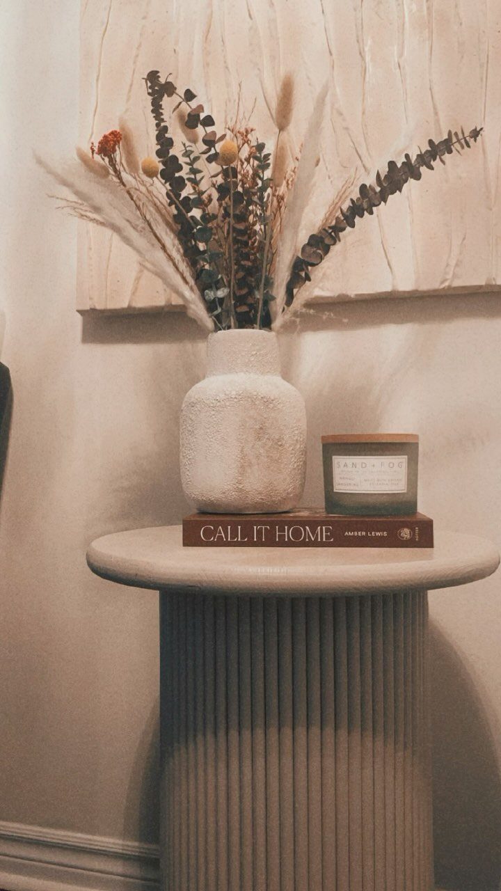 Round fluted beige end table with a white vase and dried floral arrangement
