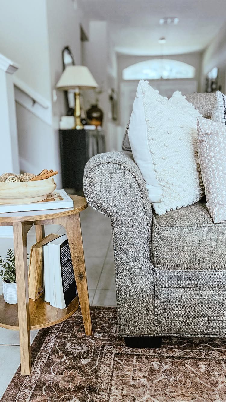 Round wooden side table with a lower shelf next to a grey armchair.