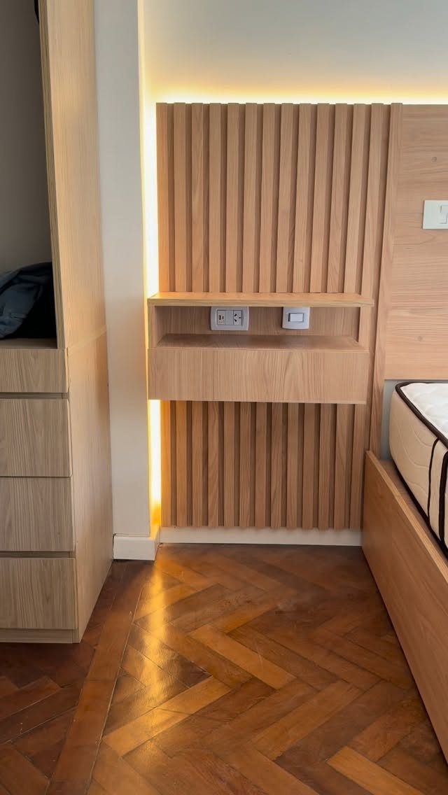 Floating wooden bedside shelf mounted on a slatted wood wall panel in a bedroom.