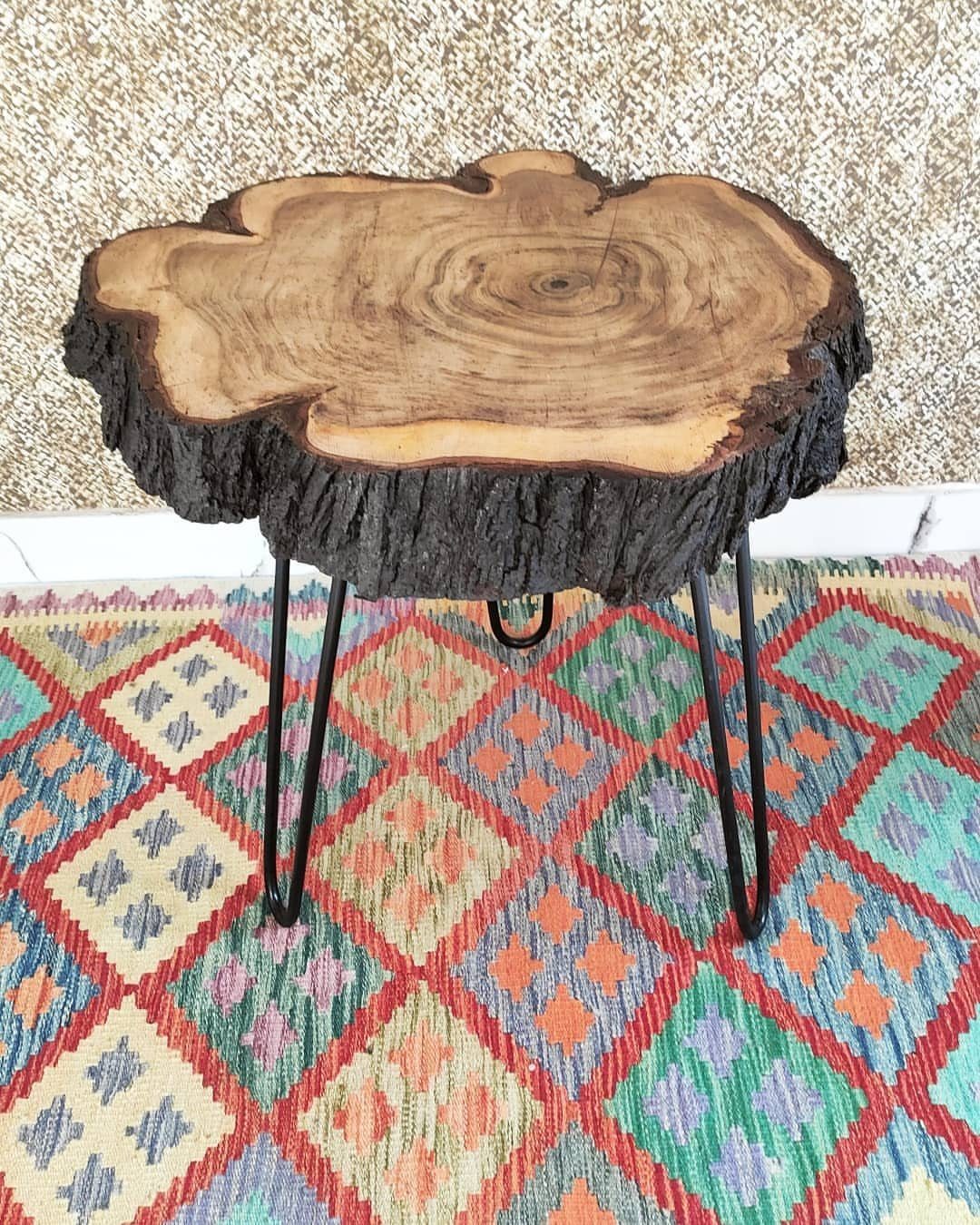 Live edge wood slice table with black metal hairpin legs on a colorful rug.