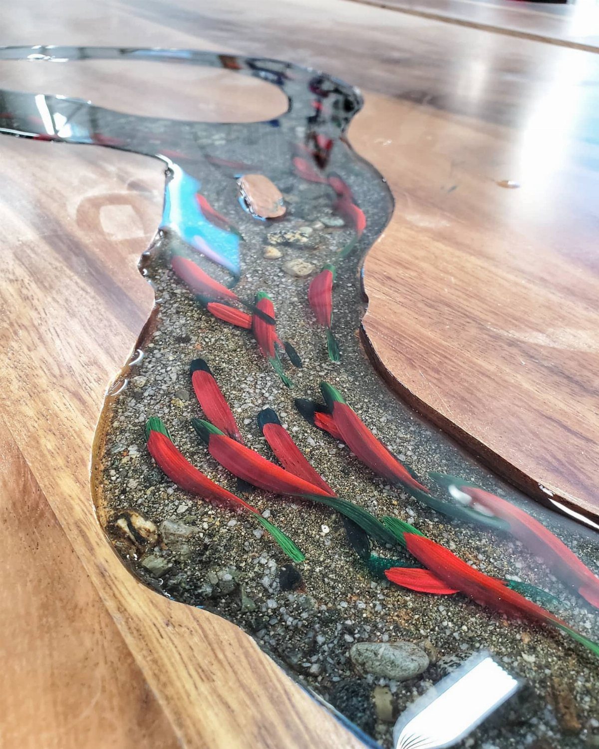 Live edge wooden table with a clear resin river containing pebbles and red accents.