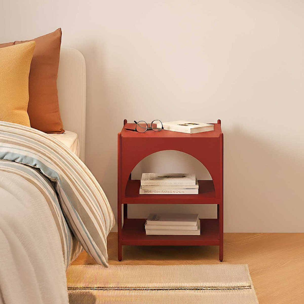 Red bedside table with arched detail and shelves next to a bed.