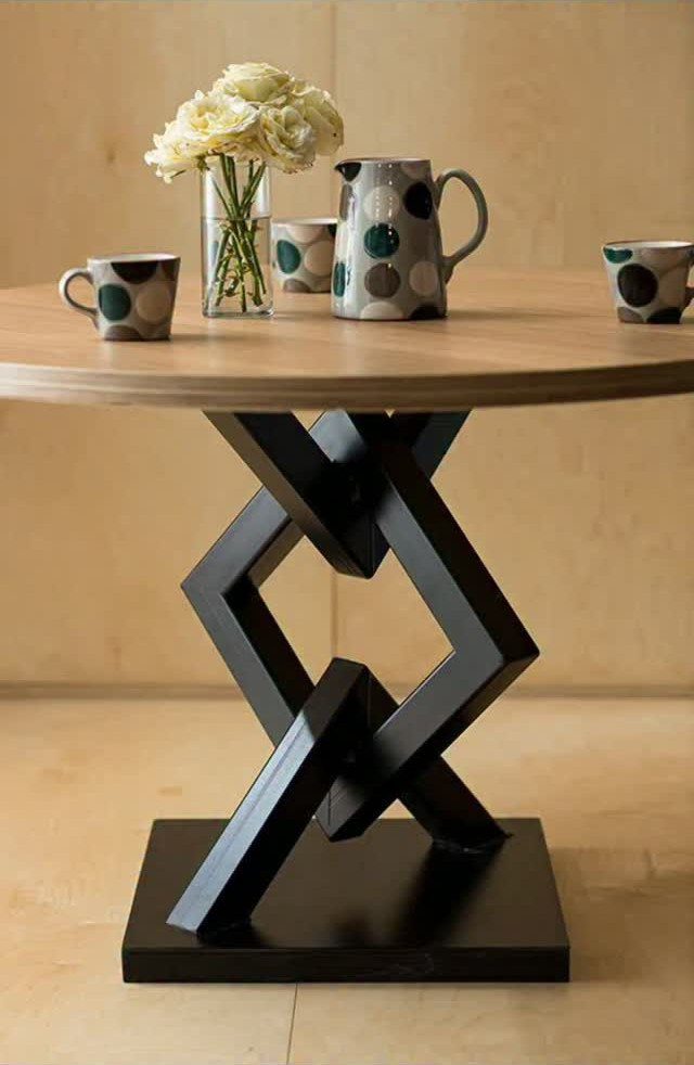Round wooden table with a black geometric base and polka dot ceramics on top.
