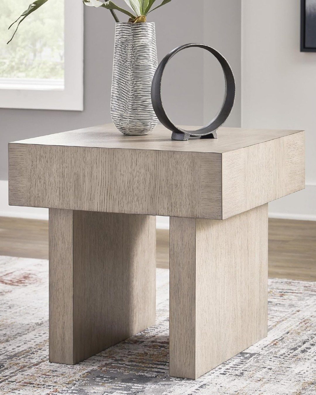 Square light wood end table with a vase and circular sculpture on top.