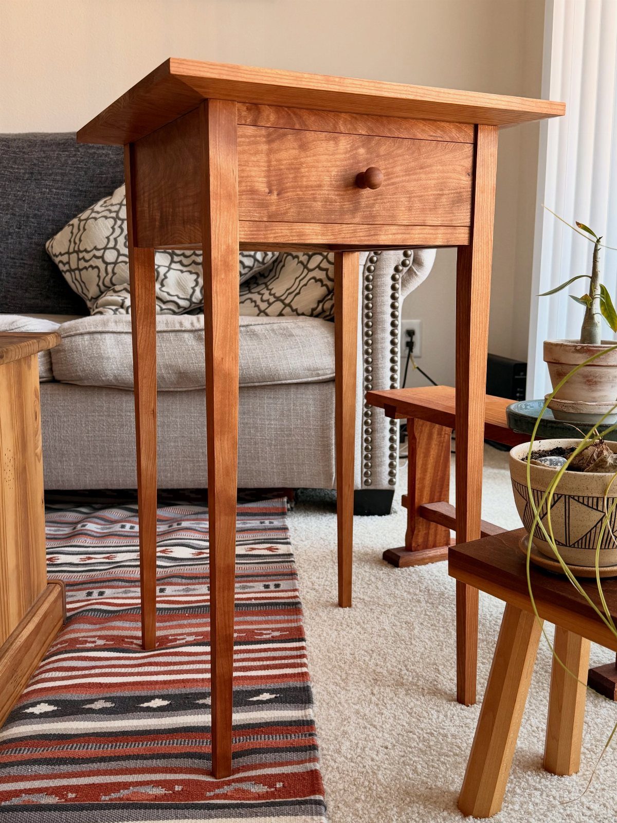 Wooden end table with a single drawer and long legs in a living room.
