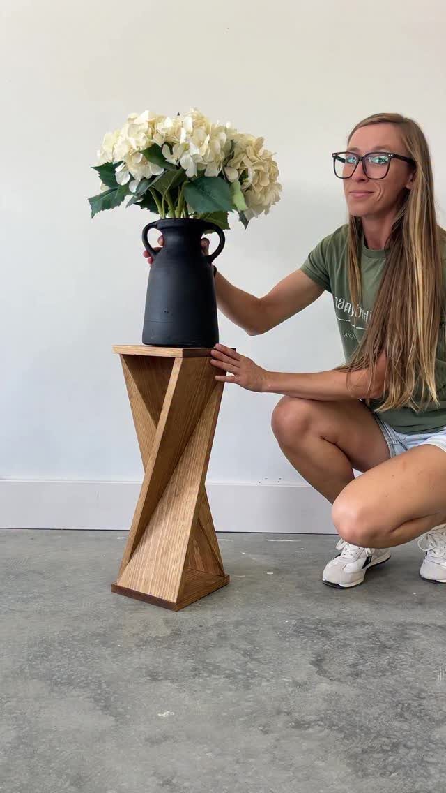 Twisted wooden end table holding a black vase with white hydrangea flowers.