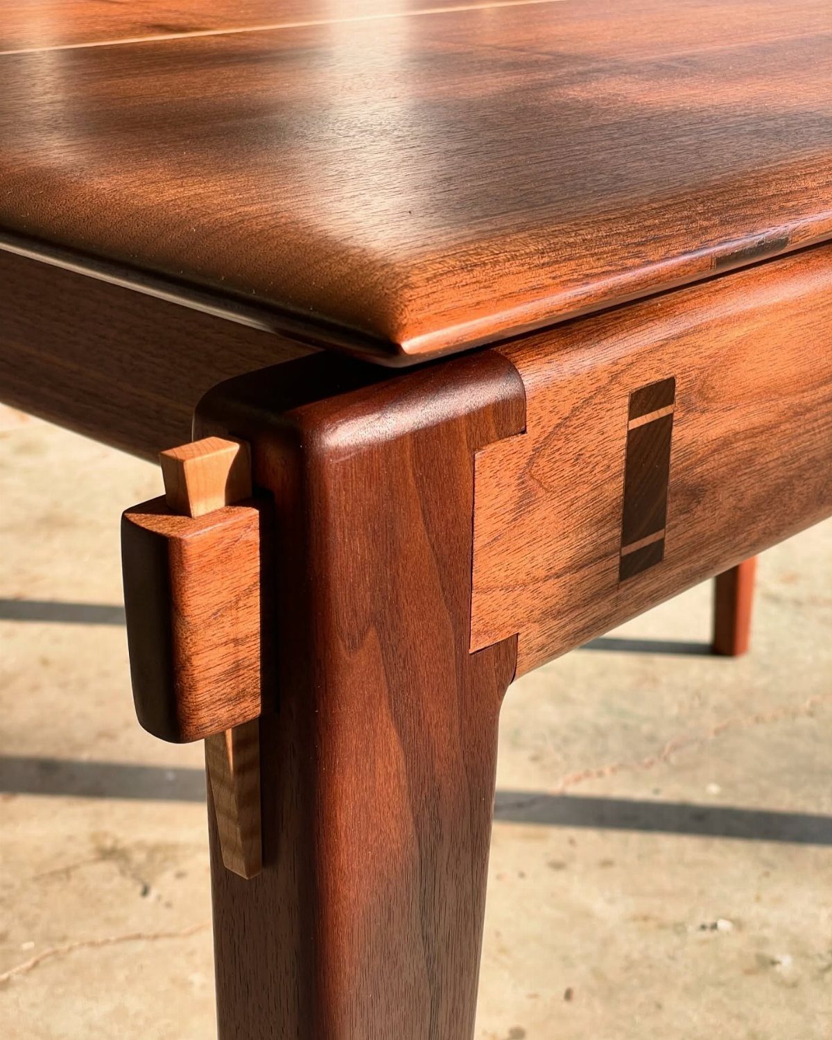 Walnut wood table corner with a contrasting light maple wood wedge joint detail.