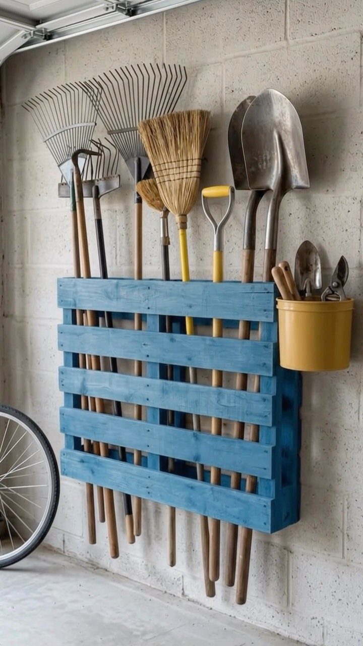 DIY Garage Organization: 17 Ideas to Build and Install 15 Blue wooden pallet tool organizer holding rakes, shovels, and brooms on a garage wall.