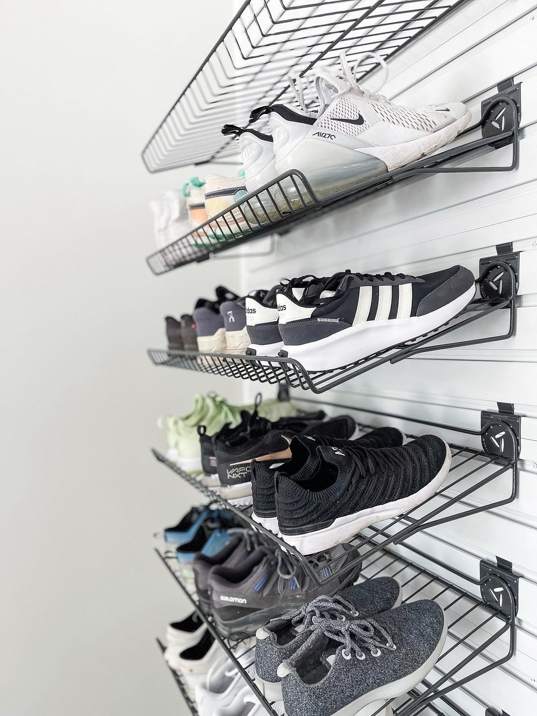 DIY Garage Organization: 17 Ideas to Build and Install 12 Black wire shoe racks mounted on a white slatted wall holding sneakers.