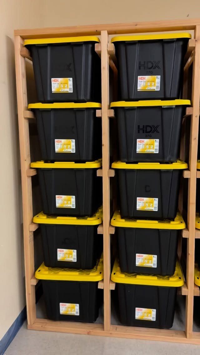 DIY Garage Organization: 17 Ideas to Build and Install 7 Black storage bins with yellow lids organized in a wooden shelving unit.