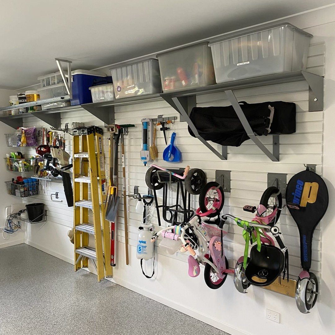 17 Garage Storage Inspiration Ideas to Organize Any Space 10 White garage wall with slatwall storage, overhead bins, bicycles, and a yellow ladder.