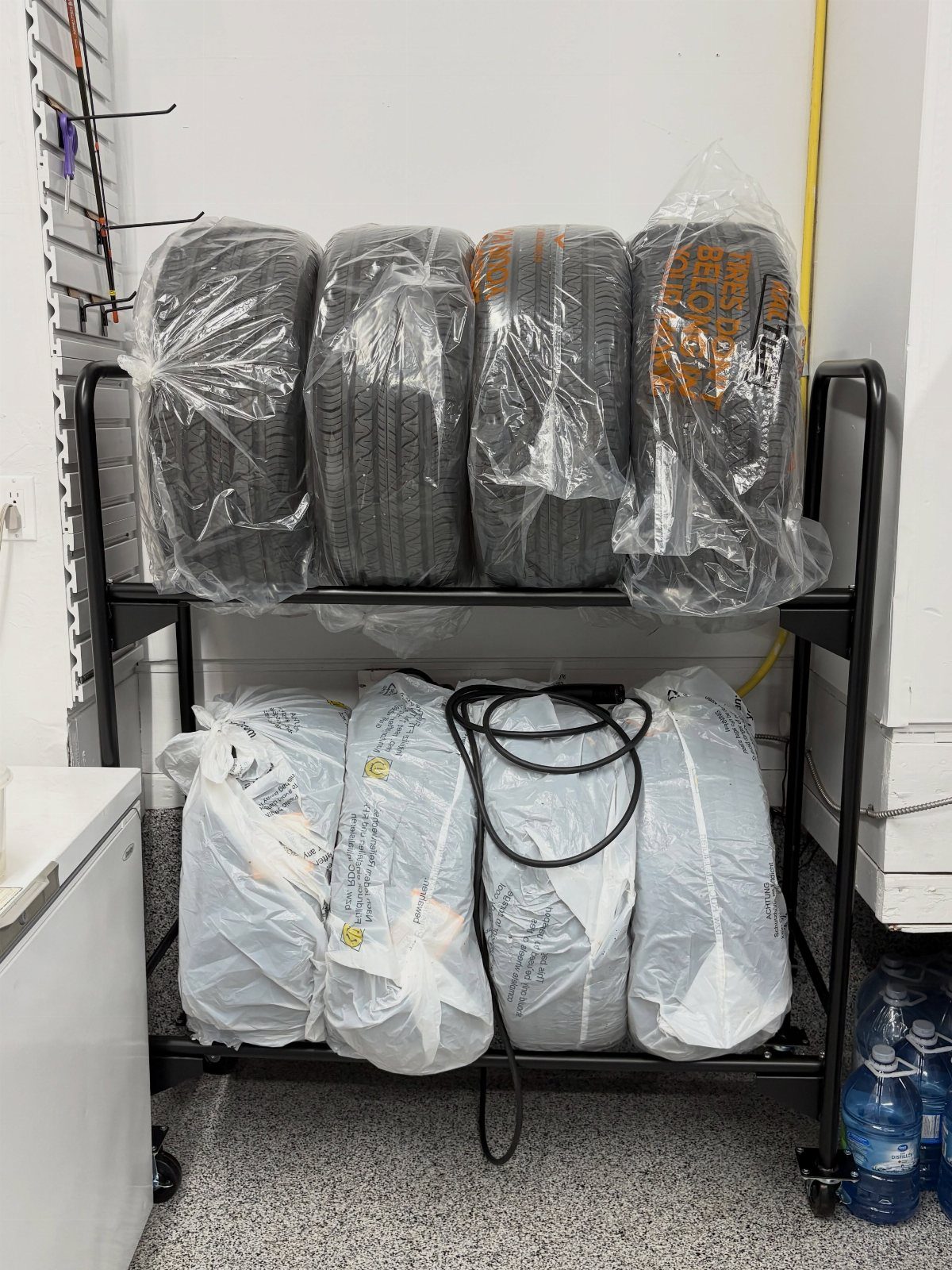 17 Garage Storage Inspiration Ideas to Organize Any Space 17 Black metal storage rack holding plastic-wrapped tires and bags in a garage.