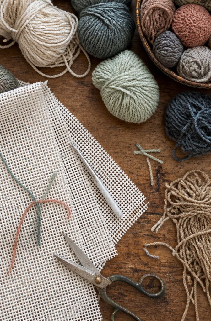 Cotton rug canvas beside a latch hook and several yarn strands