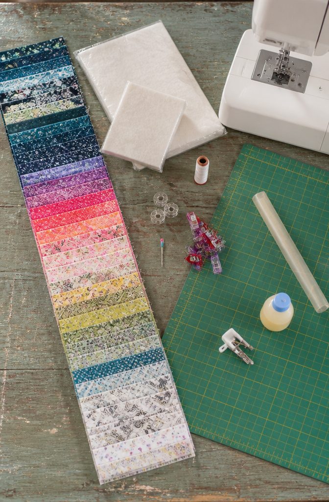 How to Make a Jelly Roll Rug (Oval, Round, or Rectangular) 1 Jelly roll strips beside batting rolls thread and a sewing machine