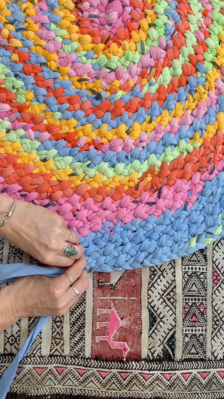Colorful circular braided rag rug being sewn by a person's hands.