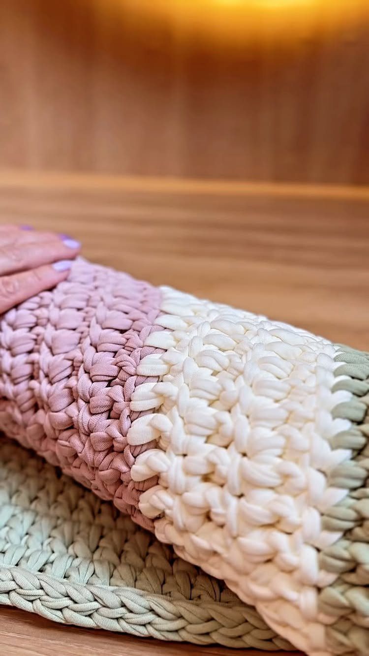 Chunky crocheted rag rug in mauve, cream, and sage green on wooden floor.