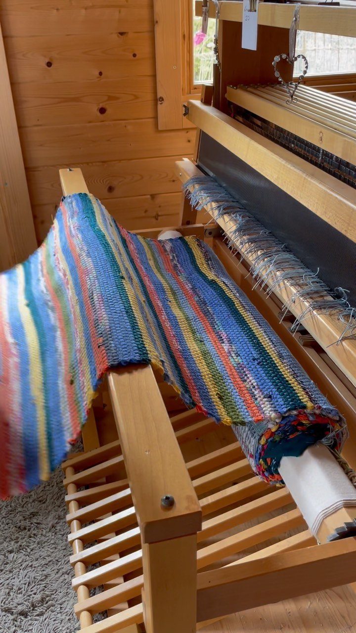 Colorful striped rag rug being woven on a wooden floor loom.