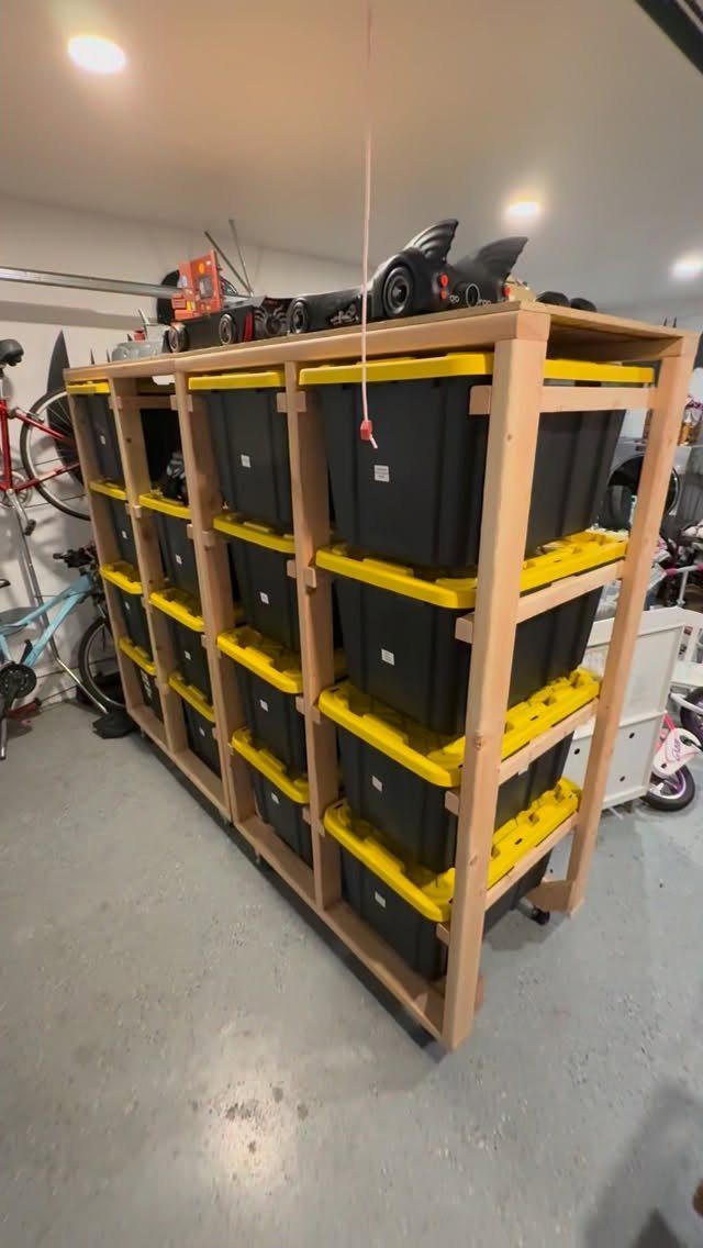 Wooden storage rack holding several black plastic totes with yellow lids in a garage.