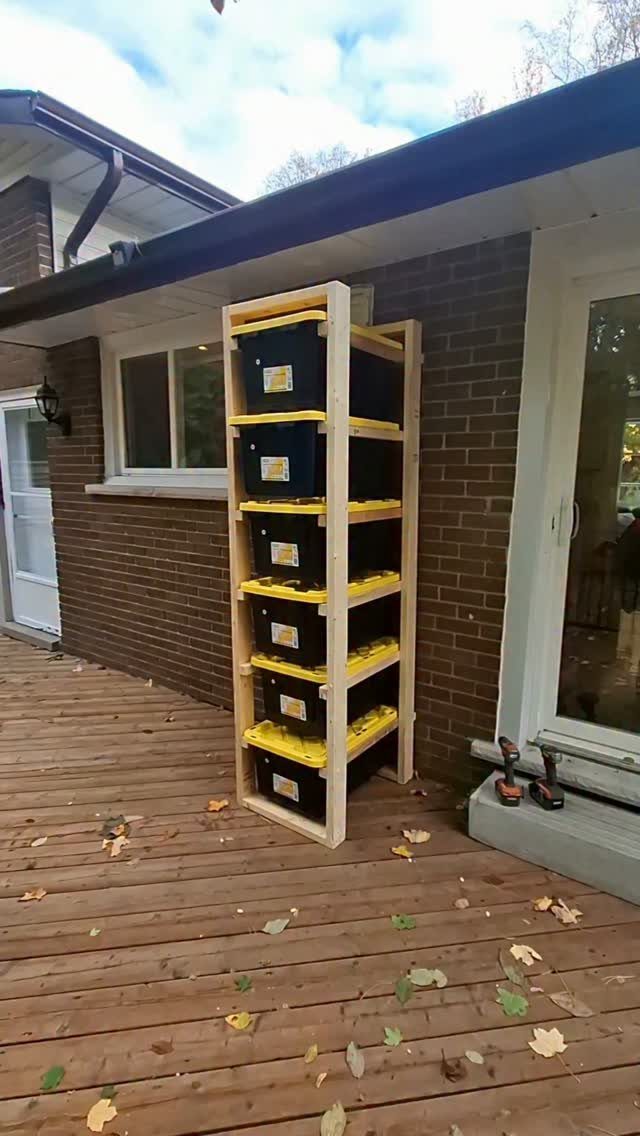 Wooden storage rack holding five black plastic totes with yellow lids on a deck.