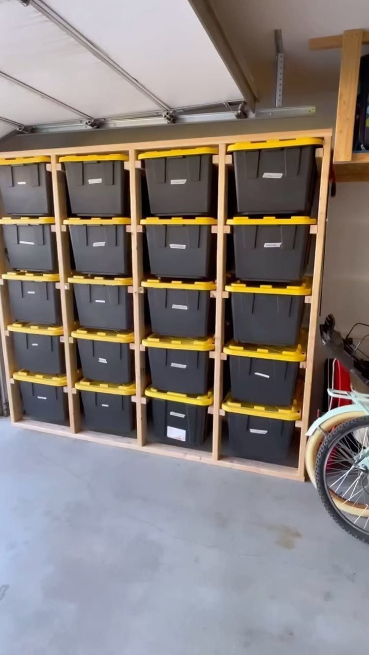 Wooden storage rack holding twenty black totes with yellow lids in a garage.