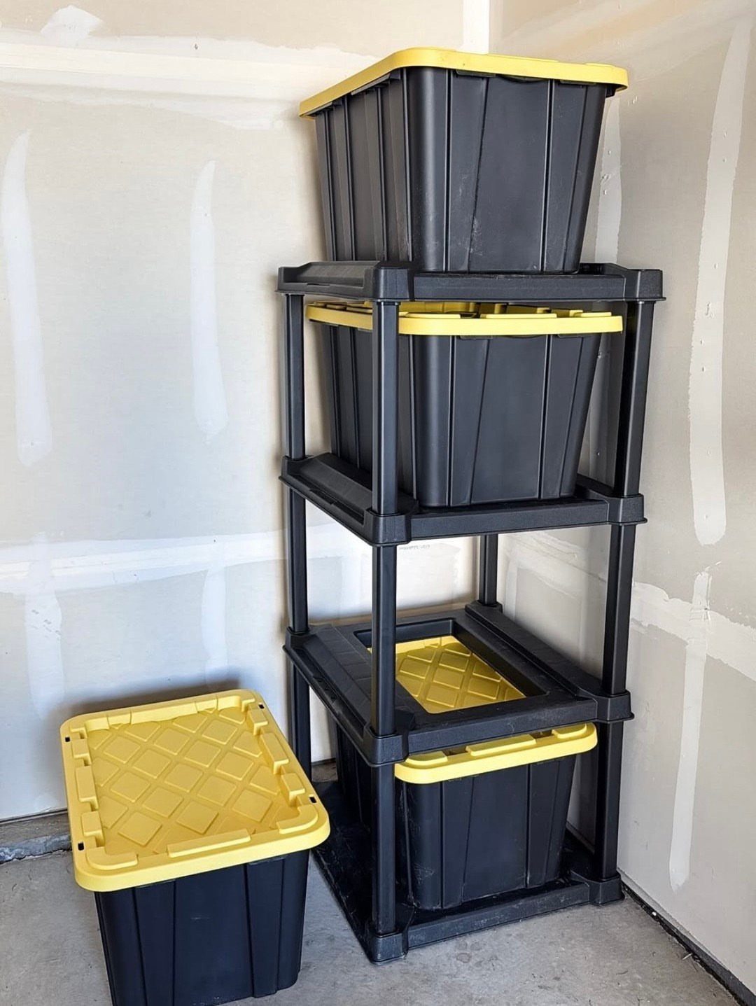 Black plastic storage rack holding black totes with yellow lids in a garage.