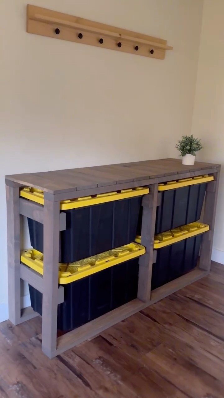 Wooden storage rack holding four black plastic totes with yellow lids in a grid.